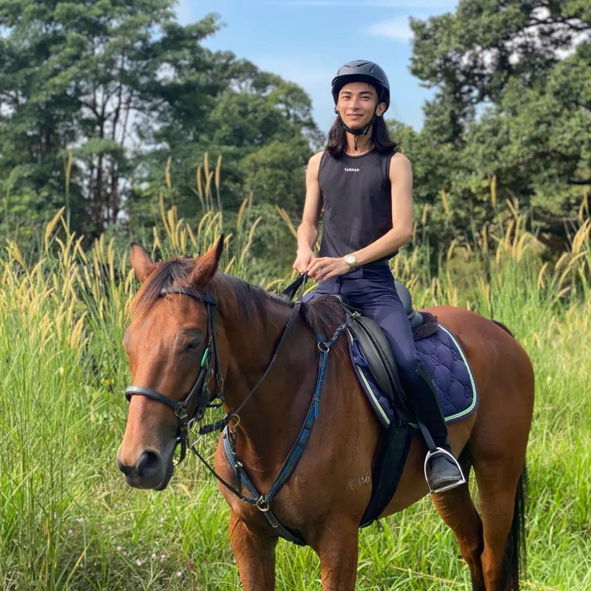 Rider on a bay horse in tall grass during a trail ride in Serdang