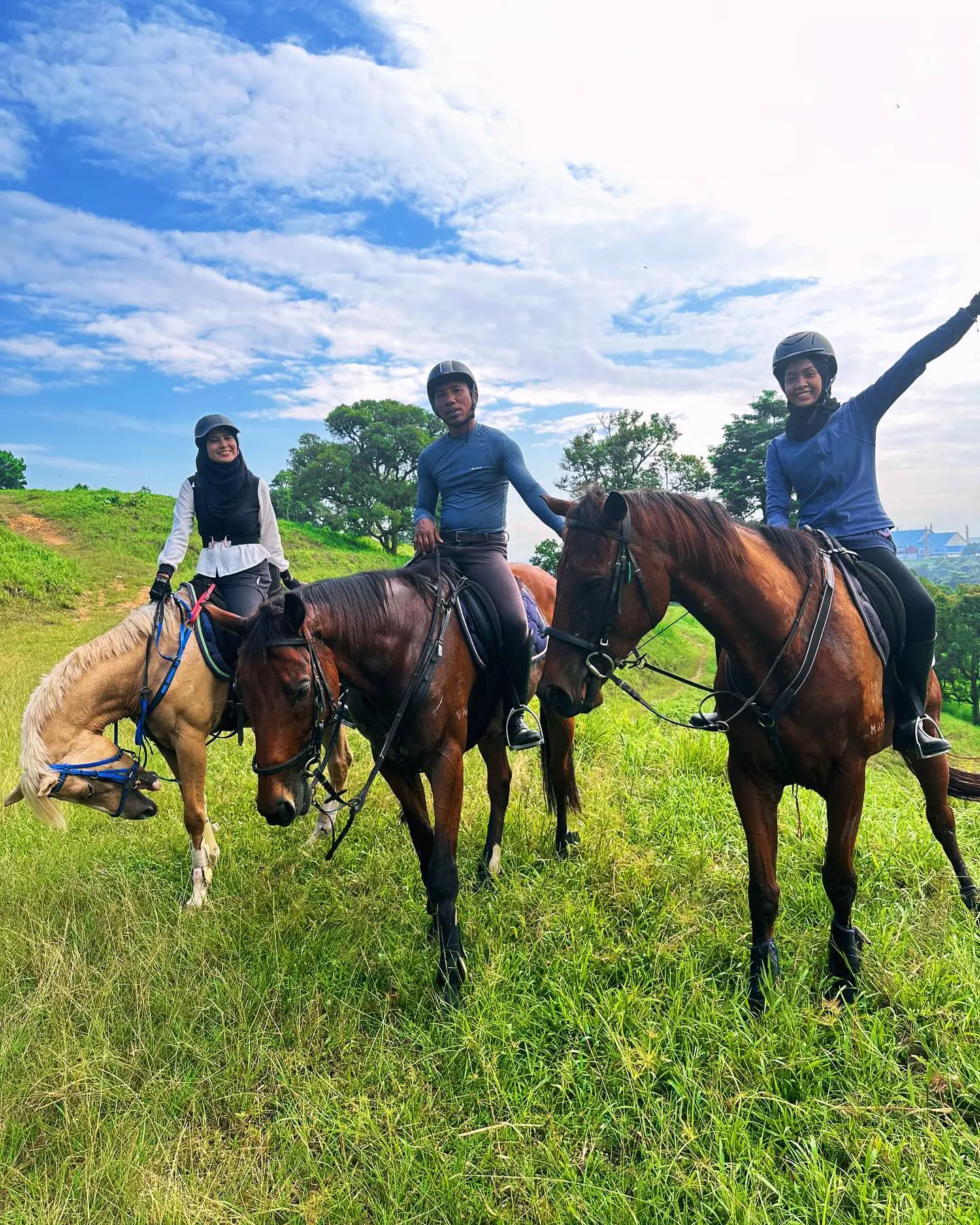 Group of three riders waving from a hilltop outride