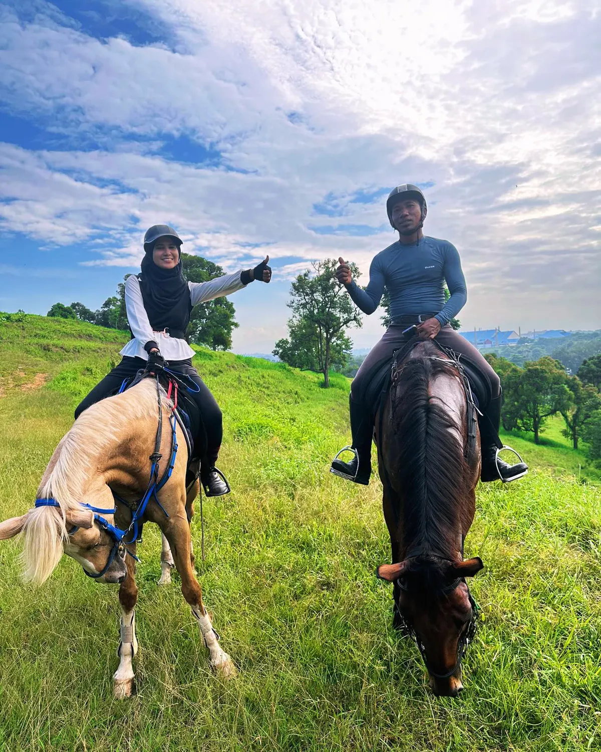 Two riders on a palomino and a bay giving a thumbs up on a pasture trail ride